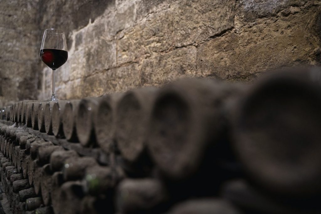 glass with red wine on aged wine bottles in vintage wine cellar